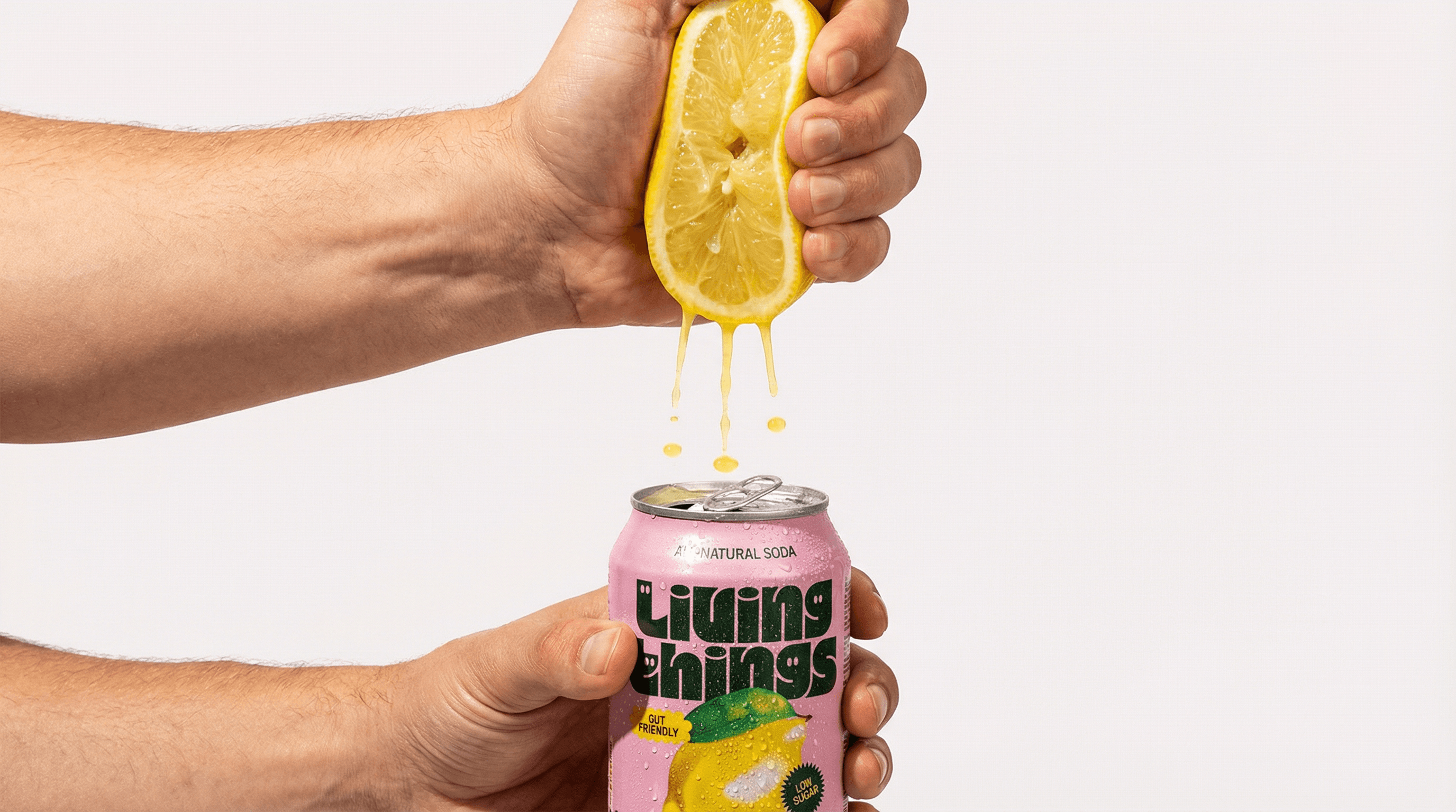 The photo is a playful, graphic product image built around gesture and cause-and-effect.
Two hands are stacked vertically against a clean, light background. The top hand squeezes a halved lemon, and juice visibly streams downward into an open pink can held by the lower hand. The moment feels frozen mid-action, emphasizing freshness, pressure, and flow.
The composition is simple but bold: fruit → liquid → can. The bright red flesh of the lemon contrasts sharply with the soft pink packaging, creating a strong visual link between flavor and product. The hands act as both functional tools and framing devices, guiding the eye through the image.
Lighting is bright and even, with crisp detail on skin texture, fruit pulp, and condensation on the can. There’s no environmental context, keeping the image clean, modern, and studio-driven.
Overall, the image feels energetic, cheeky, and contemporary, using a literal visual metaphor to communicate flavor, freshness, and immediacy in a way that’s more expressive than traditional product shots.
