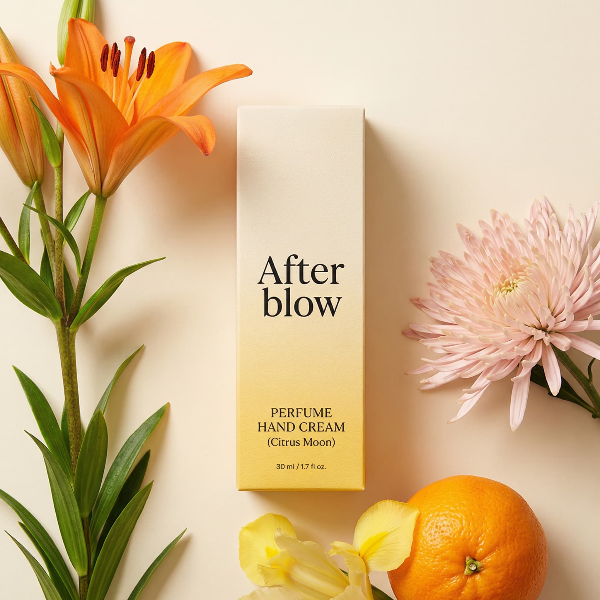 A warm and artistic beauty product photograph with botanical styling. A tall, elegant After blow 'PERFUME HAND CREAM (Citrus Moon)' package stands vertically in the center, featuring a gradient design from cream-beige at top to sunny yellow at bottom with minimalist black serif typography. The package has a subtle textured finish. Surrounding it in a carefully composed flatlay are fresh citrus-inspired botanicals: on the left, a vibrant orange lily stem with flame-colored petals and green leaves; on the right, a soft blush-pink chrysanthemum or dahlia with spiky petals; at the bottom, a bright orange citrus fruit partially visible alongside delicate yellow iris petals. Shot from directly above against a soft cream-beige background with gentle, diffused natural lighting that casts subtle shadows. The composition is balanced and editorial, with the vertical package anchoring the organic elements. The mood is fresh, luxurious, and citrus-forward—evoking sunny gardens and natural fragrance. The color palette is warm and harmonious: cream and golden yellow packaging, orange lily, blush pink flower, bright orange fruit, yellow iris, soft neutral background. The aesthetic is high-end beauty editorial—refined, natural, and sophisticated. Focus is sharp on the package typography with the flowers adding soft detail.