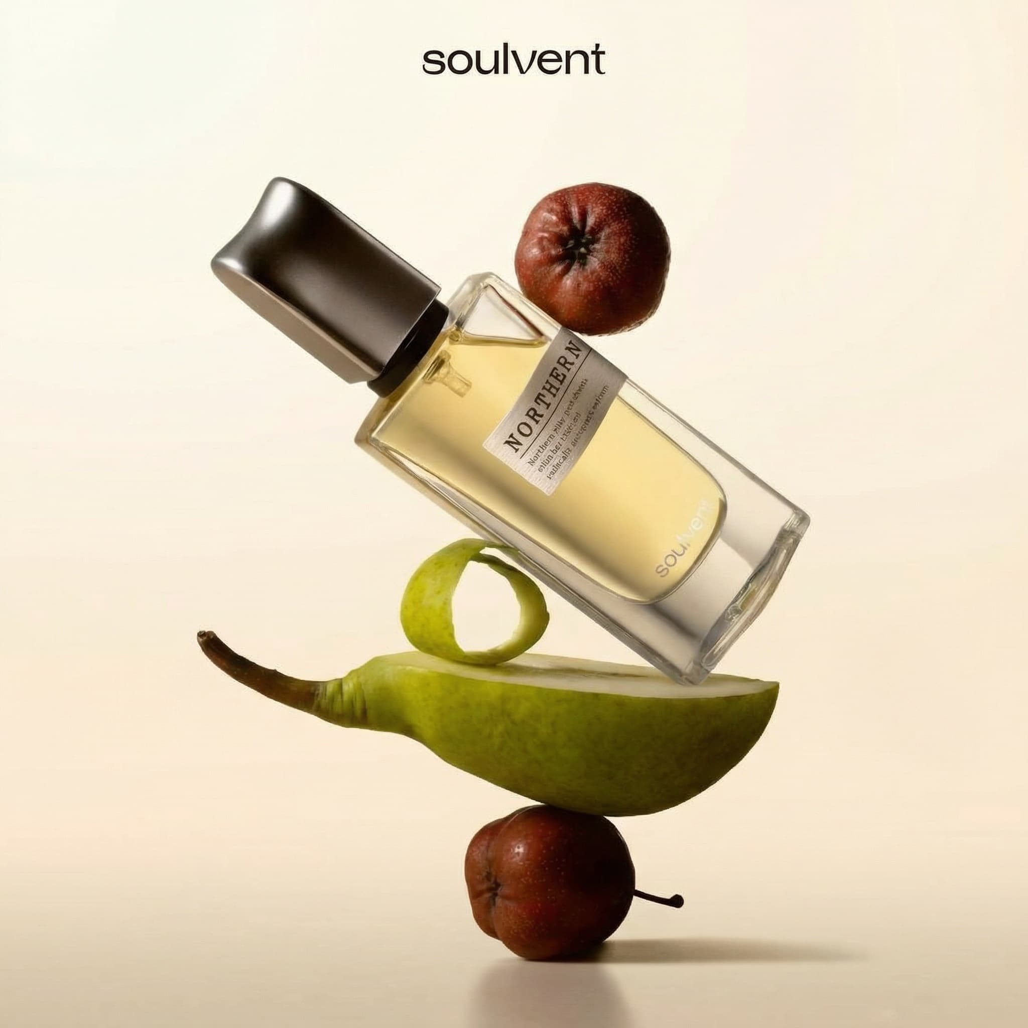 A luxury perfume bottle by Soulvent labeled NORTHERN is captured in a dynamic, gravity-defying balancing composition, tilted diagonally as it rests upon a sculptural stack of fresh fruit ingredients — a halved green pear slice with a curling ribbon of peel, a small dark red crabapple at the base, and another perched atop the bottle shoulder. The rectangular glass bottle holds pale golden liquid and features a sleek, angular matte black cap with a minimalist white label; the brand name soulvent appears in clean lowercase serif typography at the top of the frame. Shot straight-on at eye level against a warm cream-beige seamless background, the lighting is soft and diffused from the left, casting gentle directional shadows that ground the floating arrangement while maintaining an airy, editorial elegance. The color palette harmonizes autumnal greens, deep burgundy reds, and honeyed amber tones against the neutral backdrop, evoking a feeling of crisp orchard freshness and sophisticated natural artistry.