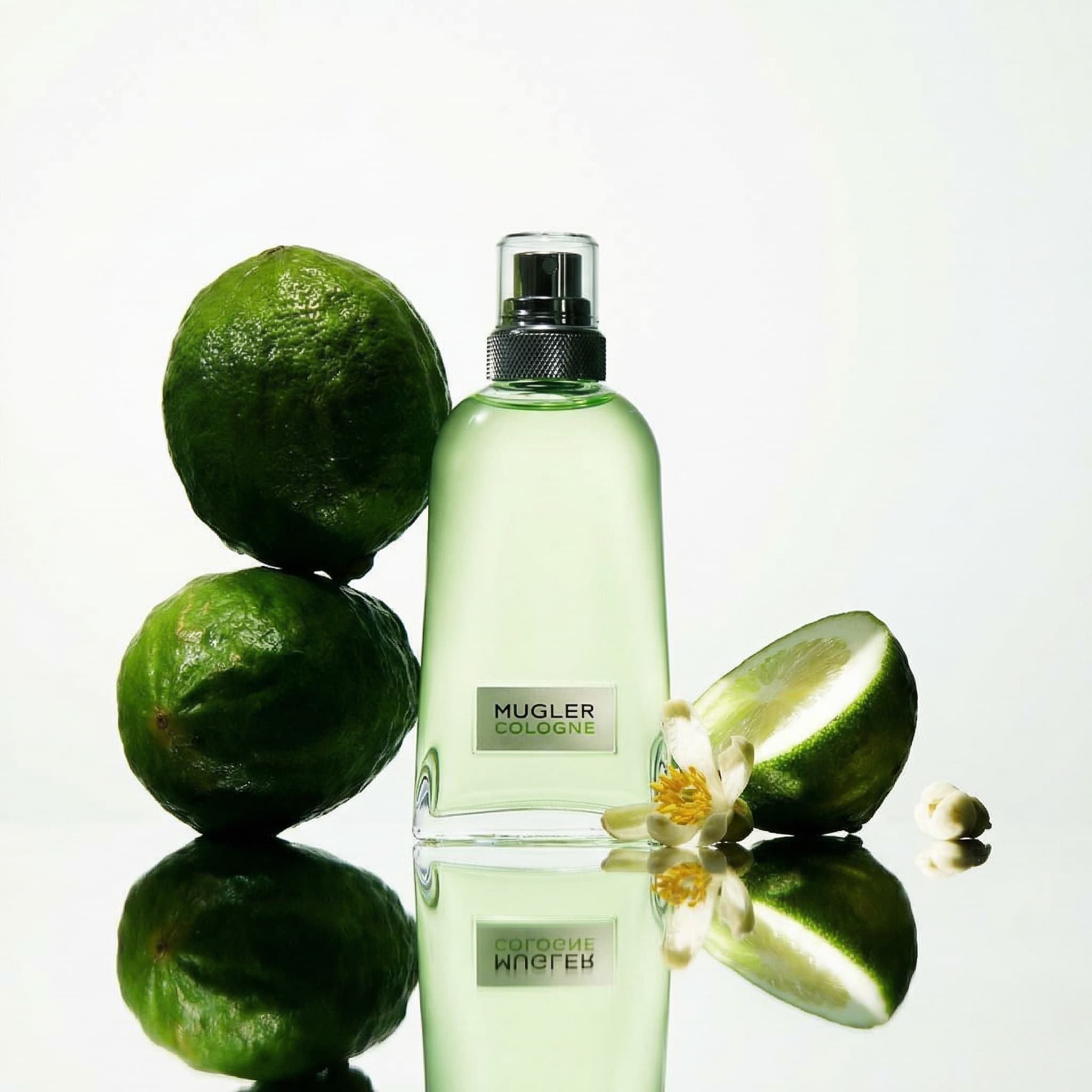 A tapered glass bottle of cologne — filled with pale green-tinged liquid, capped with a textured silver-chrome spray nozzle, and bearing a small rectangular silver label — stands centered on a highly reflective, mirror-like surface that creates perfect symmetrical reflections of every element in the scene. Two whole limes are stacked and leaning against the bottle left side, while a halved lime and a few delicate white citrus blossoms with yellow stamens rest to the right, all reflected crisply below. The lighting is bright, clean, and softly diffused from above and behind, giving the entire image a luminous, high-key glow with a cool green-white color temperature that makes the scene feel impossibly fresh, aquatic, and crystalline. The monochromatic palette of emerald greens, silvery whites, and translucent glass creates a spa-like, invigorating atmosphere — the visual equivalent of a burst of crisp citrus cologne on cool skin.