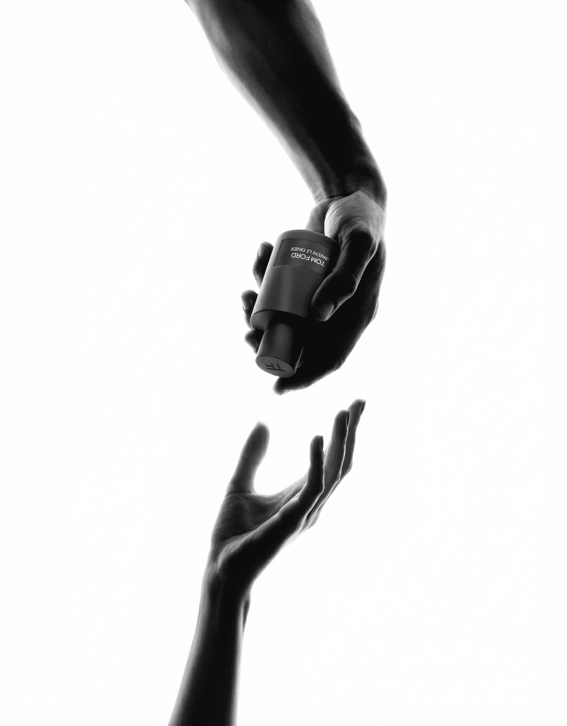 Two hands reaching toward each other in a Michelangelo Creation of Adam composition, one hand descending from above gripping a luxury dark rectangular fragrance bottle, the other rising from below with an open receptive palm. High-contrast black and white studio photography. Dramatic backlighting creates luminous rim light on skin against pure white seamless background. Sensual, editorial, high-fashion. Bold sculptural lighting emphasizing tendons, knuckles, and the tension of desire between the hands.