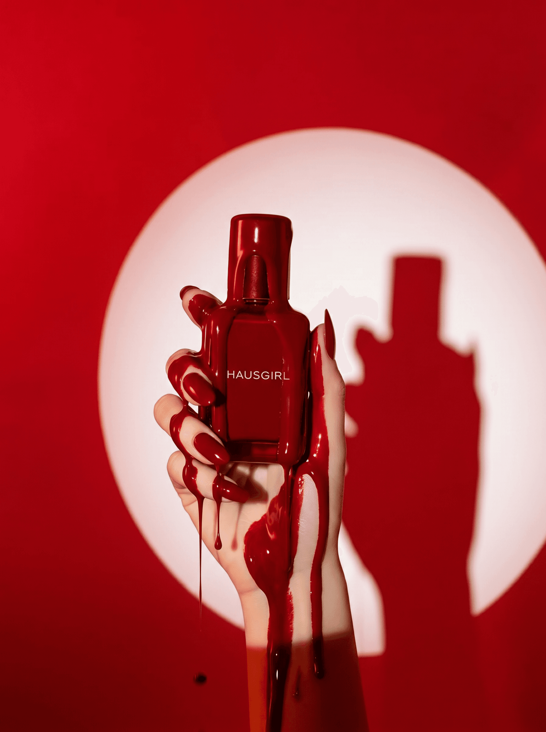 High-fashion monochromatic editorial, glossy cherry-red perfume bottle held up by a woman's hand with matching red nails, thick dramatic red liquid dripping down over her fingers, vivid red background with a circular white spotlight casting a bold silhouette shadow, theatrical luxury