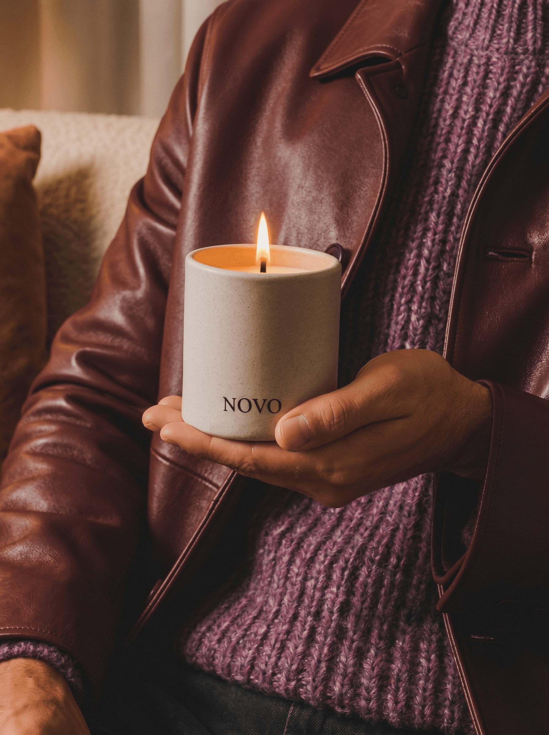 Luxurious autumnal fashion editorial, lit speckled off-white stoneware candle vessel held by a man's hand against rich oxblood leather jacket and purple marled knit sweater, warm flame glowing, tactile material contrast, lifestyle accessory with high-end sensibility