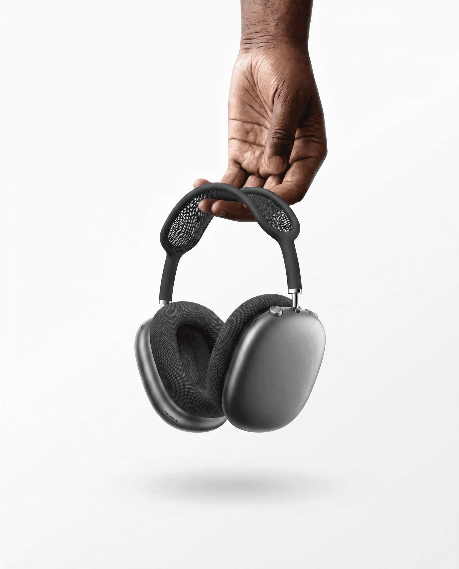 Pristine minimalist studio editorial, Apple AirPods Max Space Gray headphones held by a single hand from the headband against a pure white seamless background, classic Apple product photography lighting with soft fill and subtle gradient shadow below, the mesh canopy and aluminum ear cups rendered in crisp focus, sleek silver accents catching specular highlights, aspirational premium audio luxury