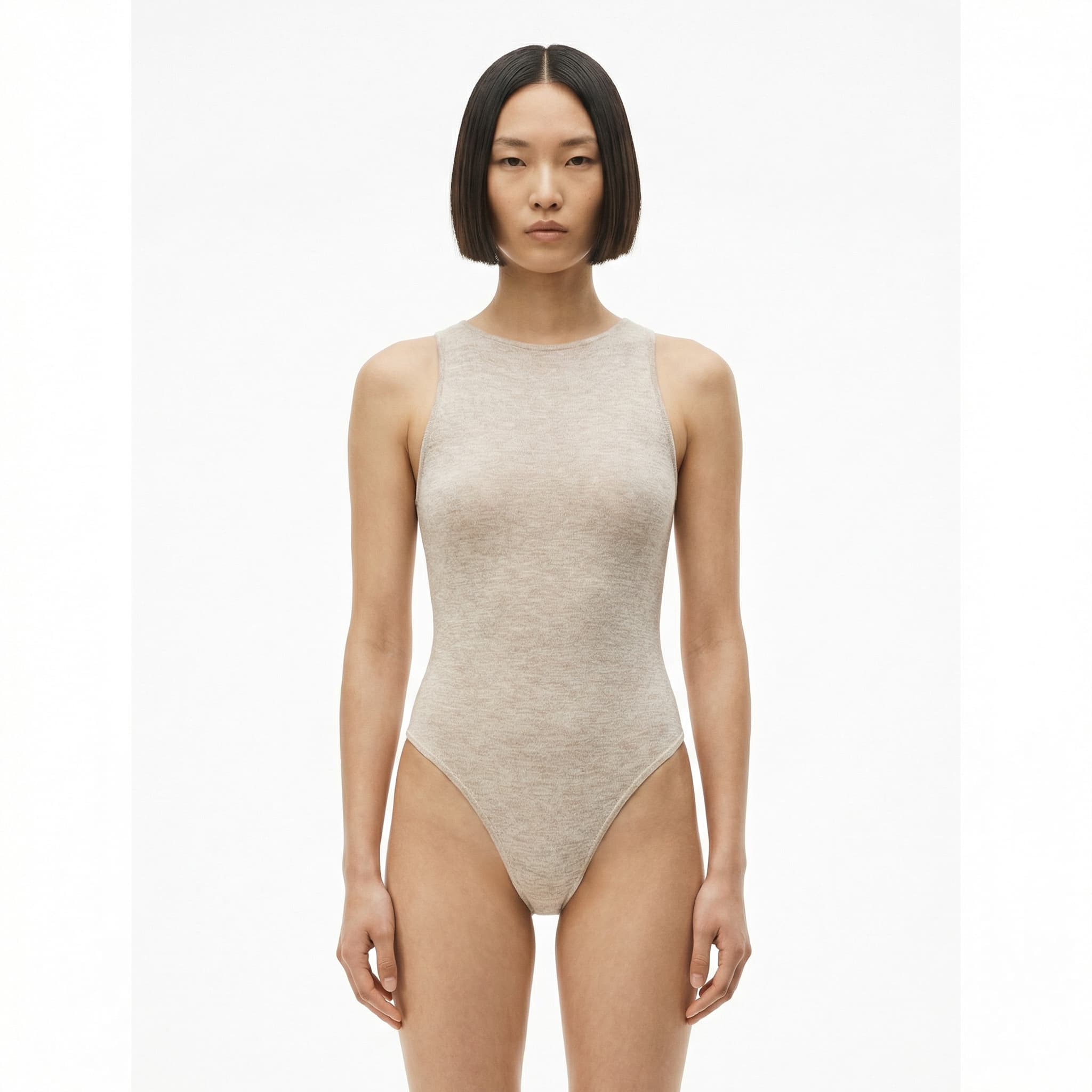 The image is a clean, body-focused fashion portrait with a minimalist, studio-driven aesthetic.
A model stands front-facing against a pure white background, centered and symmetrical in the frame. The pose is neutral and grounded, with arms relaxed at the sides, allowing the garment and body line to take visual priority over expression or movement.
The bodysuit is simple and form-fitting, with a soft, natural-toned fabric that blends closely with skin tone. This creates a near–second-skin effect, emphasizing silhouette, proportion, and texture rather than color or graphic detail. The styling is intentionally restrained—no accessories, no layering—so the focus remains on shape and material.
Lighting is bright and even, minimizing shadows and flattening contrast to present the body and garment with clarity and honesty. The model’s hair is sharply cut and symmetrical, adding a graphic counterpoint to the softness of the fabric.
Overall, the image feels modern, stripped-back, and design-centric, typical of contemporary fashion lookbooks or casting-style editorials where neutrality, proportion, and form are the primary language rather than narrative or mood.